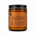 Saddle & Satin 8oz soy candle in an amber glass jar with a black lid and a leather label reading 'Saddle & Satin', hand-poured by Texas Candles.